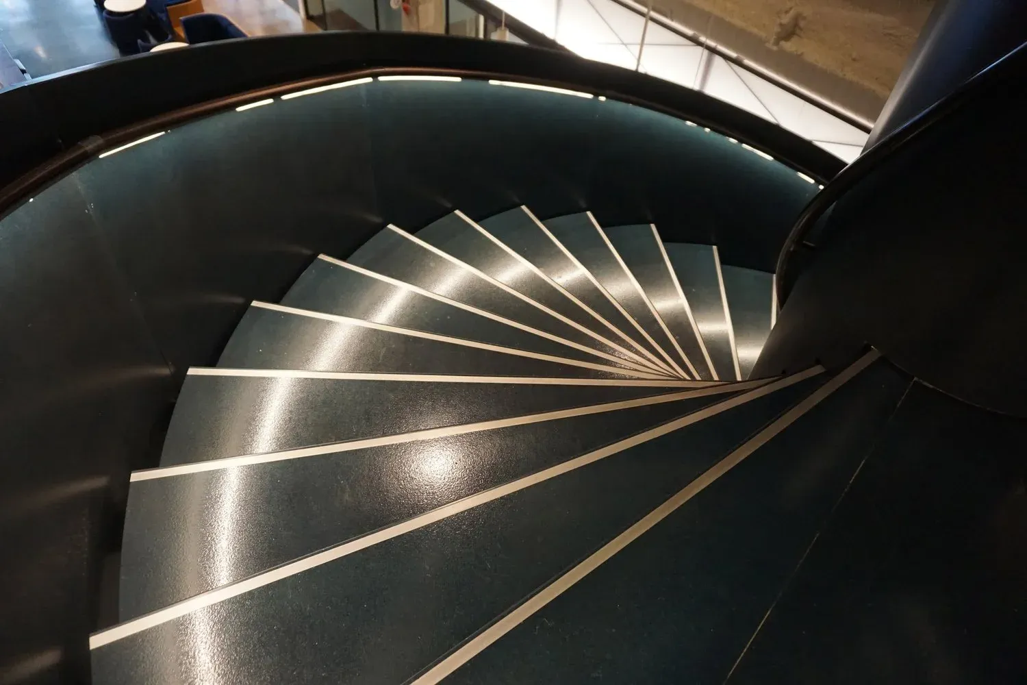The Grand Spiral Stair, a sixteen-foot-diameter helical staircase finished in a blue-toned patina, descending through the floor plate of Uber Freight's headquarters in the Old Chicago Post Office